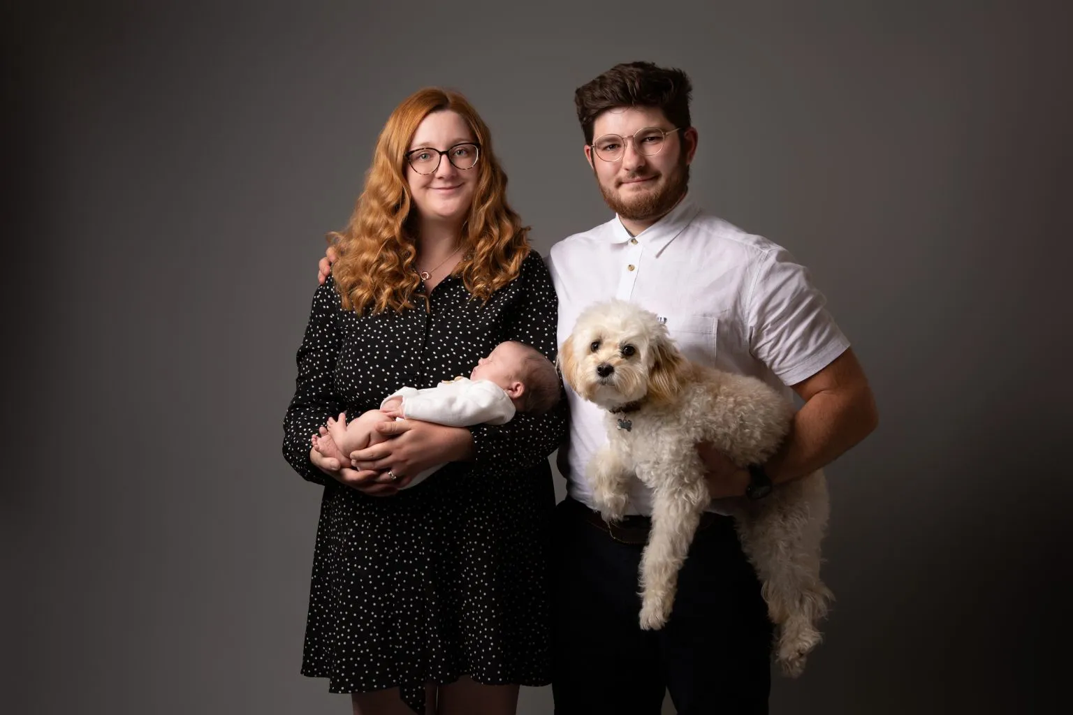 Couple holding newborn baby with small white dog